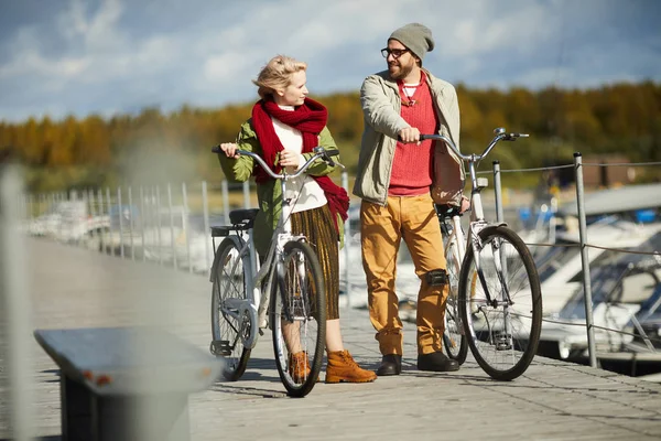 在温暖明亮的秋日下午 帅气的胡须男子穿着自行车走在码头上 与年轻漂亮的女人交谈 — 图库照片