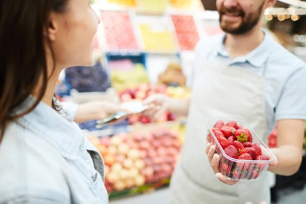 在停机坪上 积极的年轻杂货零售商的特写 拿着装满草莓的打开容器 在农贸市场给顾客品尝 他卖新鲜的草莓 — 图库照片