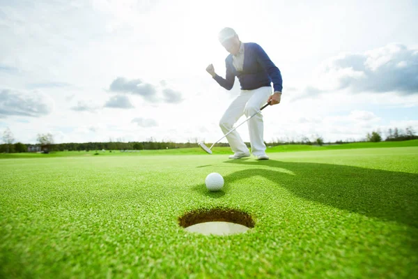 緑のフィールドに立ってそれを見ながらゴルフボールを打つアクティブな男 — ストック写真