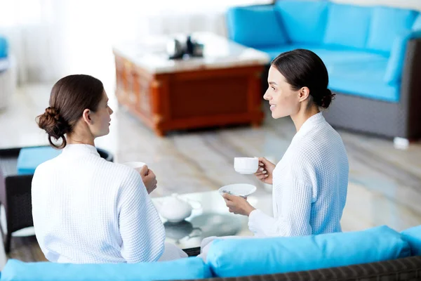 Two Girls White Bathrobes Sitting Sofa Talking Cup Tea Coffee — Stock Photo, Image