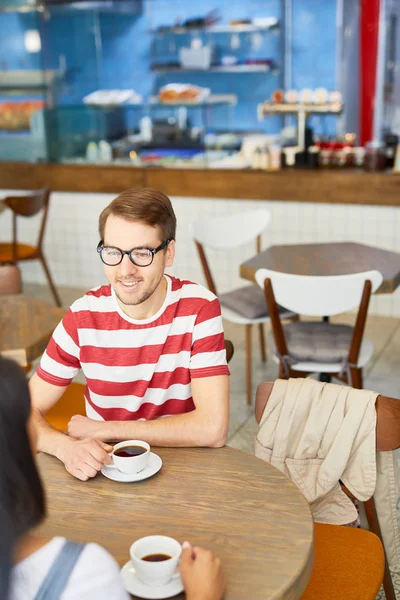 カフェでコーヒーを飲みながら会話中に同僚を見ているカジュアルなTシャツを着た若いビジネスマン — ストック写真