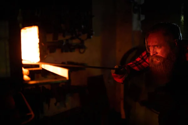 そこに鉄の工作を置きながら炉の燃える火を見てひげ鍛冶屋 — ストック写真