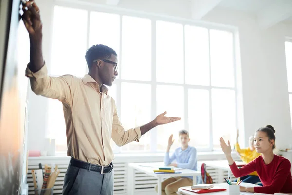 自信的年轻非洲裔美国老师指着黑板 同时与中学生在上课 — 图库照片