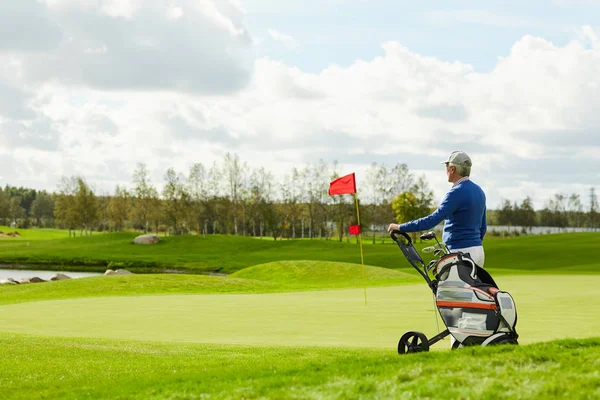 夏の週末に大きな緑のプレイフィールドに立ってスポーツバッグと高齢者のゴルフ選手 — ストック写真