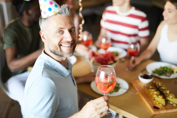 Cheerful mid-aged man looking at camera with smile while cheering up at birthday party