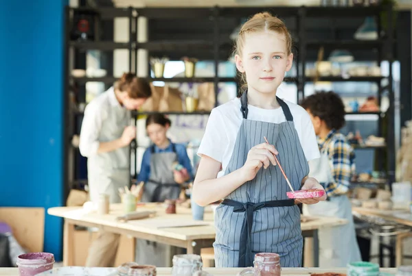 レッスンで陶器を塗る前にプラスチック皿に色を混ぜたペイントブラシを持つ小さな女の子 — ストック写真