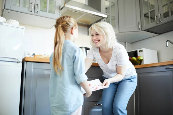 Cheerful mother taking handmade card from her daughter hands and giving thanks for the gift