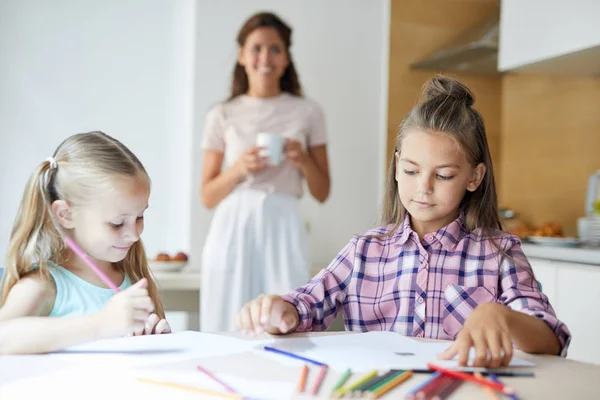 年轻姑娘们 穿着蜡笔画 与妈妈一起坐在厨房的桌子旁 背景上画画 — 图库照片