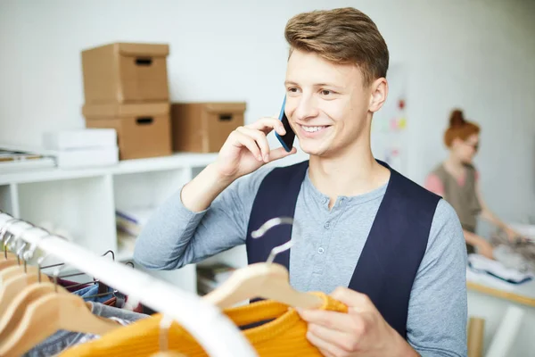 Sorrindo Jovem Estilista Falando Telefone Celular Escolhendo Roupas Para Ordem — Fotografia de Stock