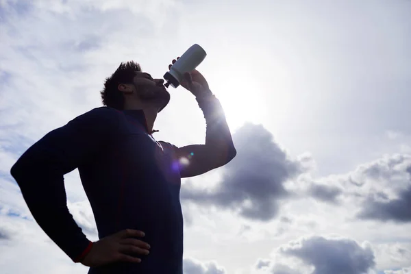 Aktivní Člověk Pije Vodu Plastové Láhve Proti Zatažené Obloze Slunci — Stock fotografie