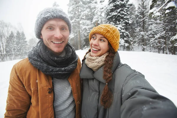 微笑兴奋的女孩爱上了男朋友看着他 而他们采取自拍在冬季森林 — 图库照片