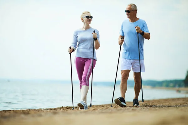 朝の砂浜の海岸線に沿って楽しいアクティブな高齢者のカップルトレッキング — ストック写真