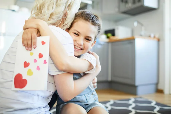 Sorrindo Menina Com Cartão Saudação Artesanal Abraçando Sua Mãe Cozinha — Fotografia de Stock