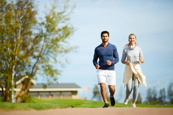 朝の自然環境の中で一緒に走るアクティブウェアの幸せなカップル — ストック写真