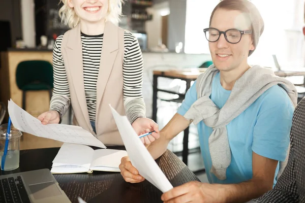 Warm toned portrait of contemporary businessman wearing glasses and beanie hat smiling cheerfully and holding document while working with colleagues during meeting in modern office, lens flare