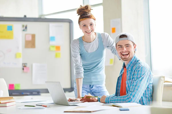 Dos Jóvenes Compañeros Alegres Mirándote Por Lugar Trabajo Mientras Trabajas — Foto de Stock