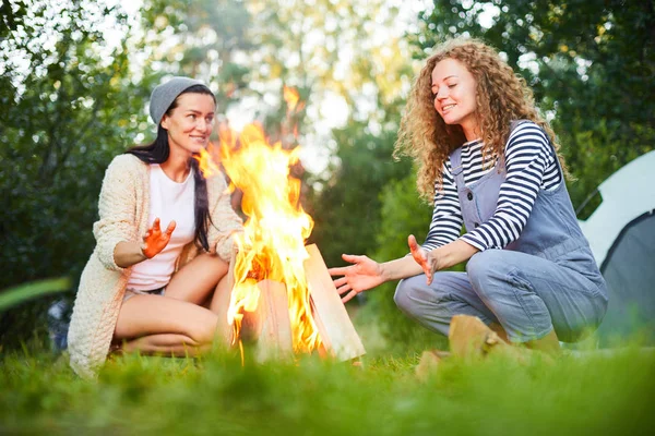 两个年轻女子坐在篝火旁 晚上说话取暖 — 图库照片