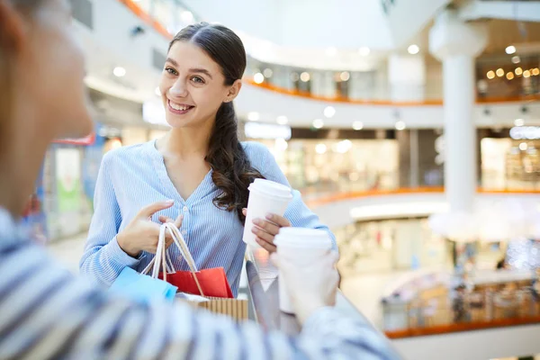 飲み物とショッピング バッグ販売中のショッピング モールで彼女の友人に話しての束と笑顔の女の子 — ストック写真