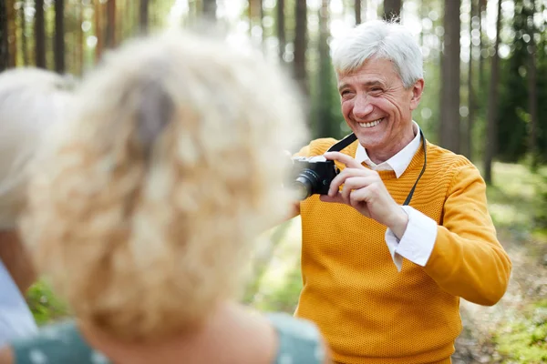 乔利兴奋英俊的中年男子穿着黄色毛衣拍摄朋友相机和笑 同时要求他们在森林中摆姿势 — 图库照片