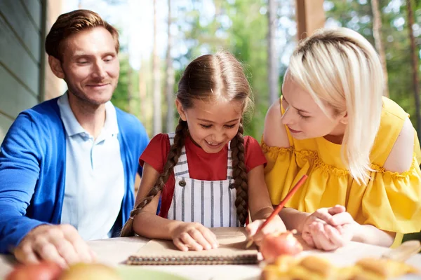 Chica Feliz Dibujando Bloc Notas Entre Sus Padres Mientras Relaja — Foto de Stock