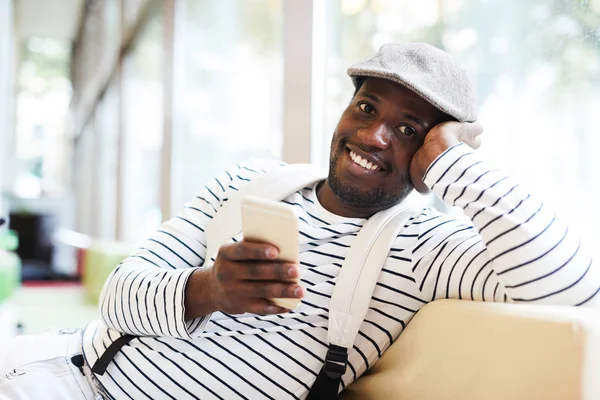 穿着便服 面带微笑的年轻人在休息时坐在窗边 用智能手机发短信 — 图库照片