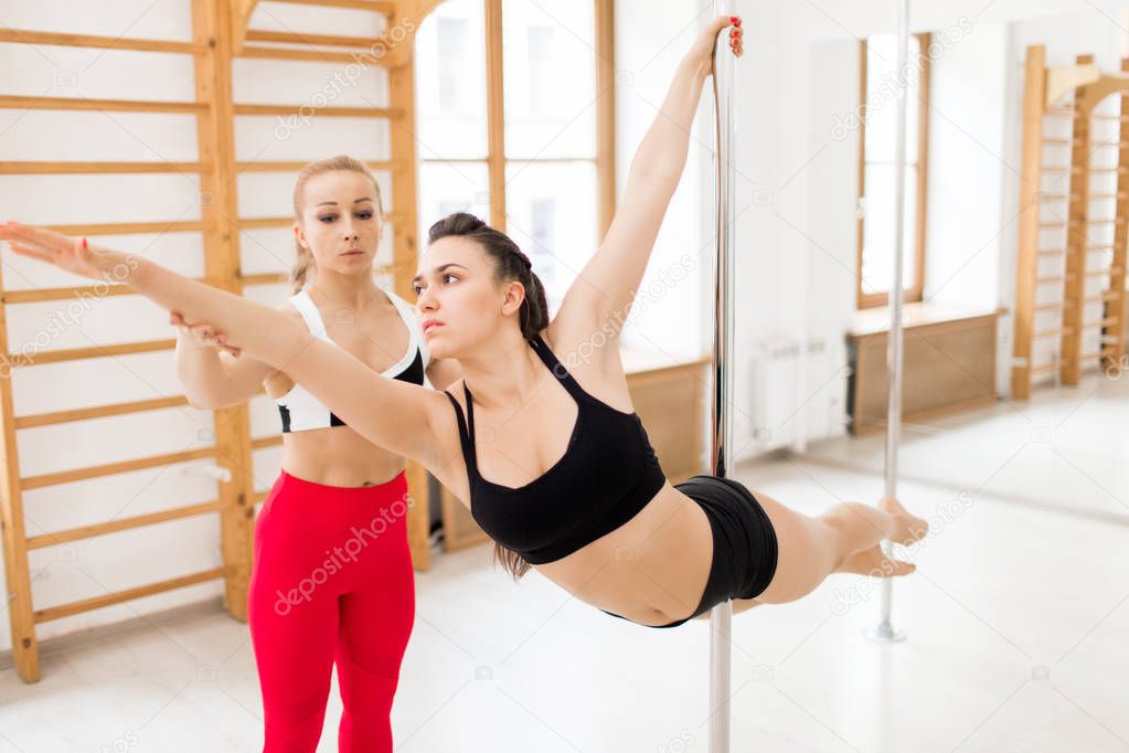 Young active woman doing gymnastics on pole while professional coach helping her