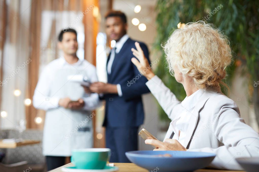 Blonde businesswoman calling for waiter while sitting at the restaurant at business lunch