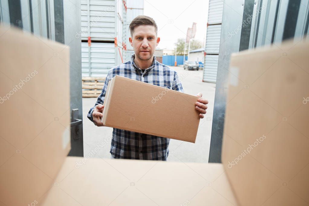 Serious handsome man loading container with boxes and putting it on stack of packages