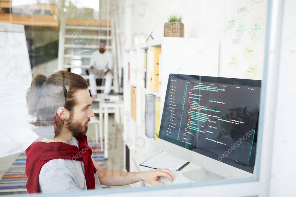 Serious programmer looking at coded data on computer screen while sitting in front of it