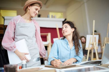 Stüdyoda çalışma anlarını tartışırken birbirlerine bakan iki arkadaş canlısı kız