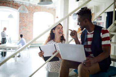 Genç bayan ofis çalışanı, modern ofiste iş gününde iş arkadaşıyla eğleniyor.