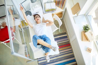 Masa başında yatan, en sevdiği müziği dinleyip ofiste şarkı söyleyen rahat giyimli kendinden geçmiş genç yönetici