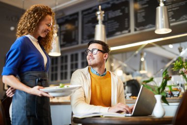 Genç garson müşterilerden birine siparişi getiriyor. Masa başında oturuyor ve ağ kuruyor.
