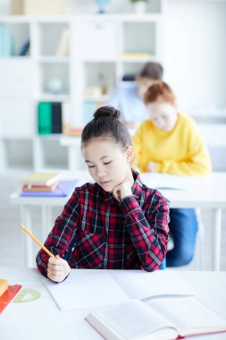 Sınıfta masa başında oturan ve çizim yaparken copybook boş sayfasına bakarak boya kalemi ile pensive küçük kız