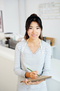 Asyalı etnik kökenli genç garson kafeteryada sipariş alırken not defterine not alıyor.