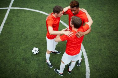 Kucaklayan ve yeşil alan üzerinde dururken daire yapma üç genç futbolcular