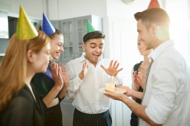 Heyecanlı genç adam arkadaşları tarafından sunulan doğum günü pastası parçası şaşırtıcı bakıyor