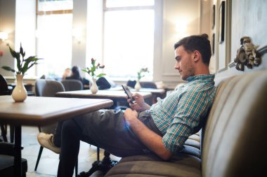 Yeni konukları beklerken ve akıllı telefonunda mesajlaşma yaparken masa başında kanepede oturan rahat garson
