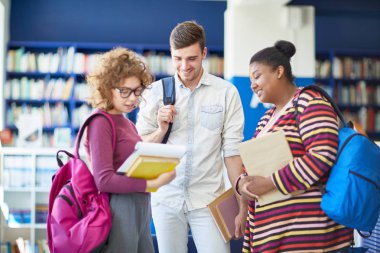 Üniversite kütüphanesinde birlikte duran ve kitap tartışan öğrenci grubu