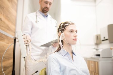 Young patient with electrode on head and her doctor controlling the procedure