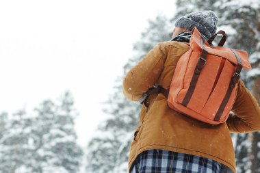 Kış ormanında kar altında yürüyen ve yürüyüşte doğayı düşünen turuncu sırt çantalı erkek sırt çantalı nın arka görünümü