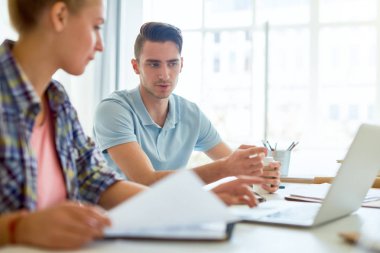 Genç kendine güvenen bir adam, meslektaşına modern iç tasarımın bazı özelliklerini açıklarken dizüstü bilgisayarını işaret ediyor.