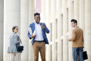 Video bağlantısı üzerinden konuşan ve konuşma hakkında heyecanlı planı ile Neşeli yakışıklı siyah mühendis, iş adamları yürürken ona bakıyor