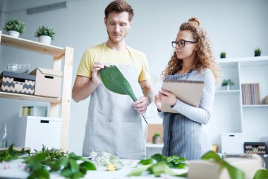 Yeni demet oluştururken yeşil yaprakları ile çalışan iş elbisesi iki genç çiçek tasarımcıları