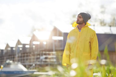 İçerik dalgın dalgın su geçirmez ceket ve şapka genç adam etrafa bakıyor ve sonbaharda iskelede yürürken güneşli bir gün zevk