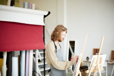 Çalışan genç bir sanatçı resim yapmak için resim sehpasının önünde duruyor.