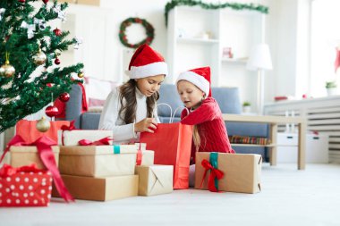Noel Baba şapkalı sevimli kardeşler yerde hediye kutuları arasında kırmızı paperbag bakıyor