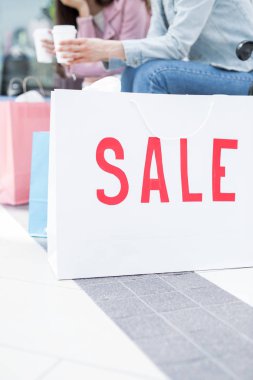 Kırmızı fark büyük çağdaş merkezi yerde beyaz paperbag satışa ve arka plan üzerinde içecekler ile iki kız