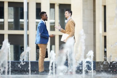 Çeşmenin yanında duran ve açık havada çalışma anlarını tartışan zarif takım elbiseli iki kültürlerarası adam