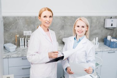 Tıbbi belgelerle çalışırken kameraya bakan üniformalı iki başarılı klinisyen